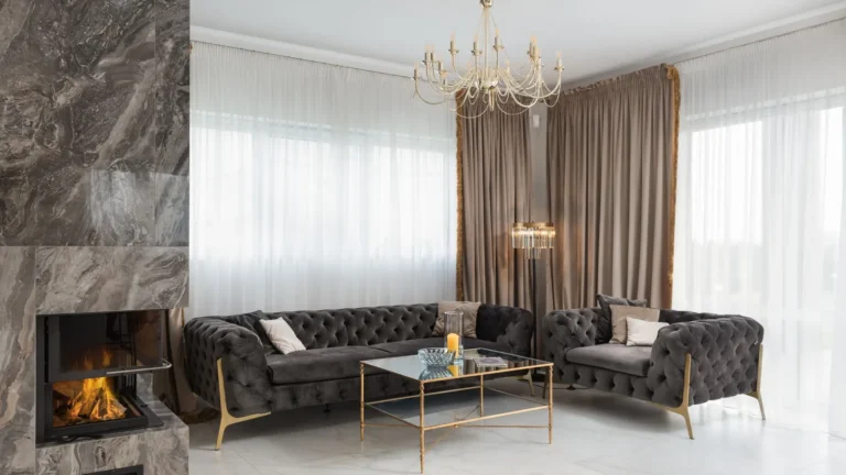 Marble-clad lounge with a fireplace, chandelier and a gray tufted sofa