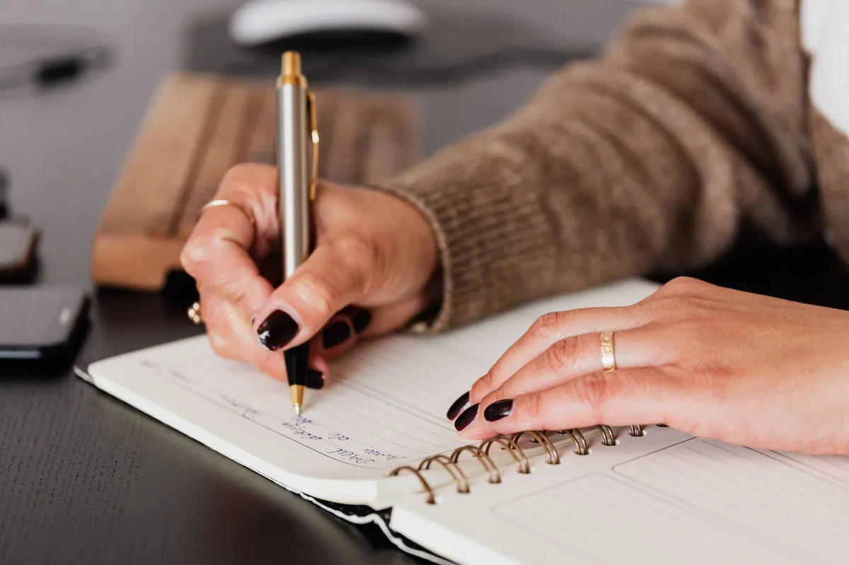 Close view of hands writing in a spiral notebook at a dark desk