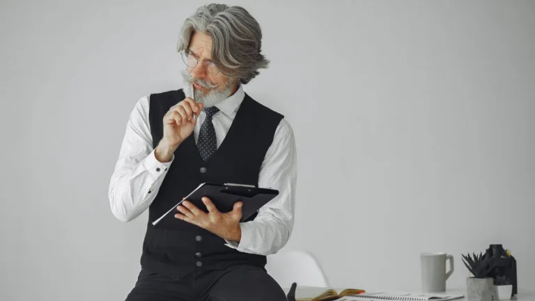 Senior man with gray hair holding a tablet while thinking through a plan at his desk