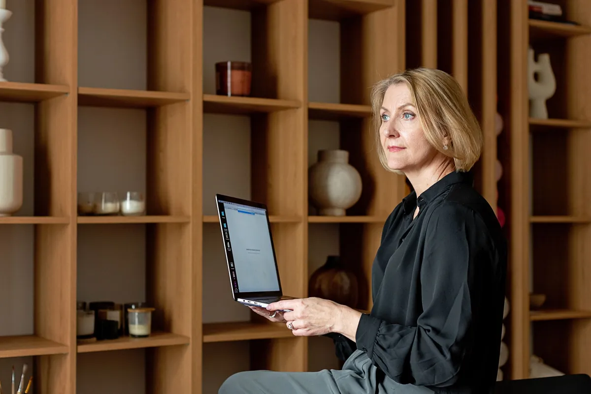 Woman in a black blouse working on a laptop in a home office with warm wood shelving
