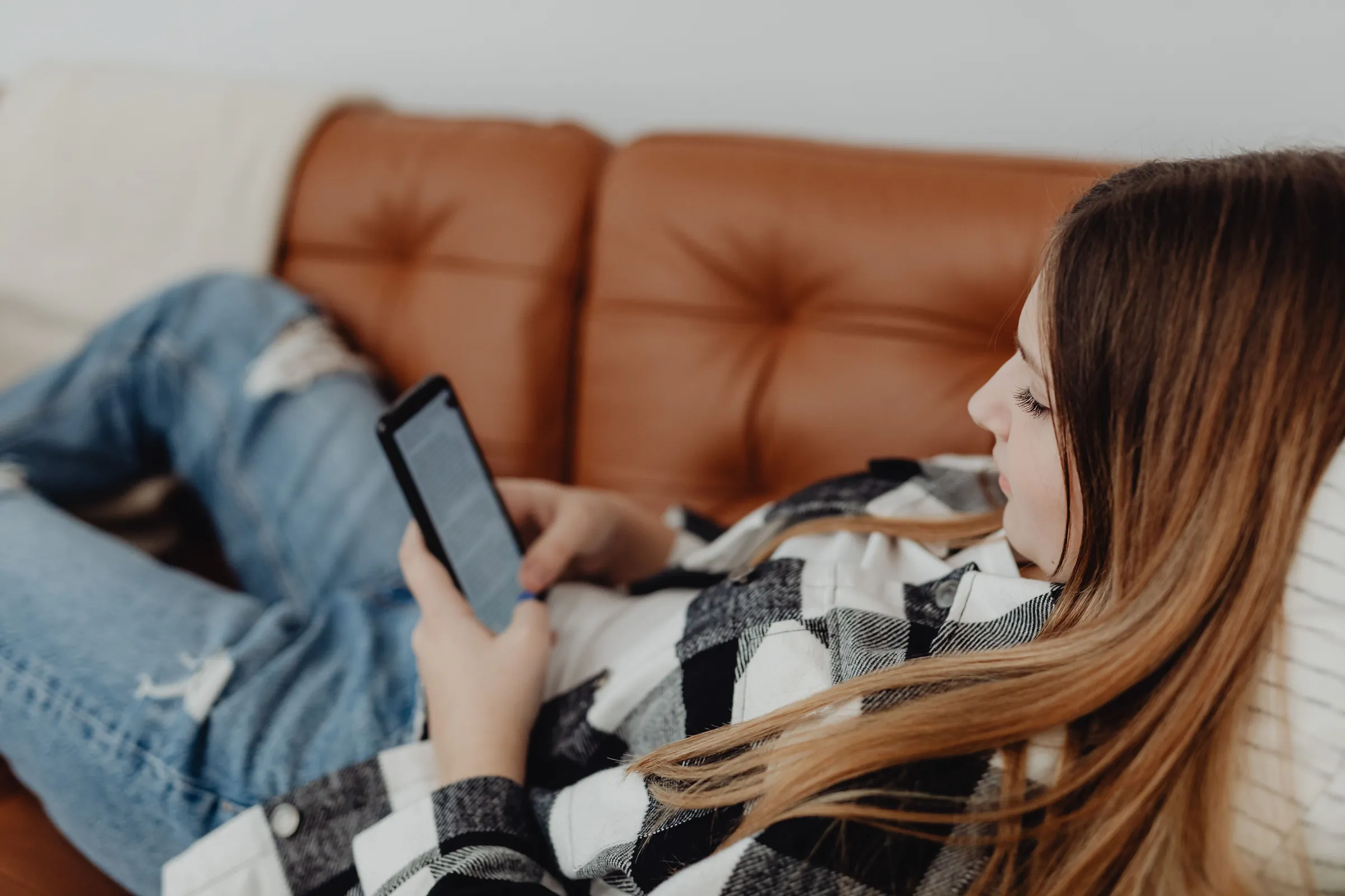 Woman relaxing on a leather sofa while texting on her phone, illustrating patients messaging a practice through Google's AI agent