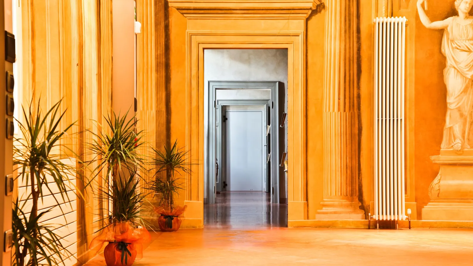 Sunlit palazzo doorway framed in ochre plaster, palms and a marble statue