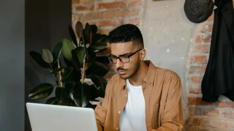 Practice owner in glasses working on a laptop in a cafe with brick walls and plants