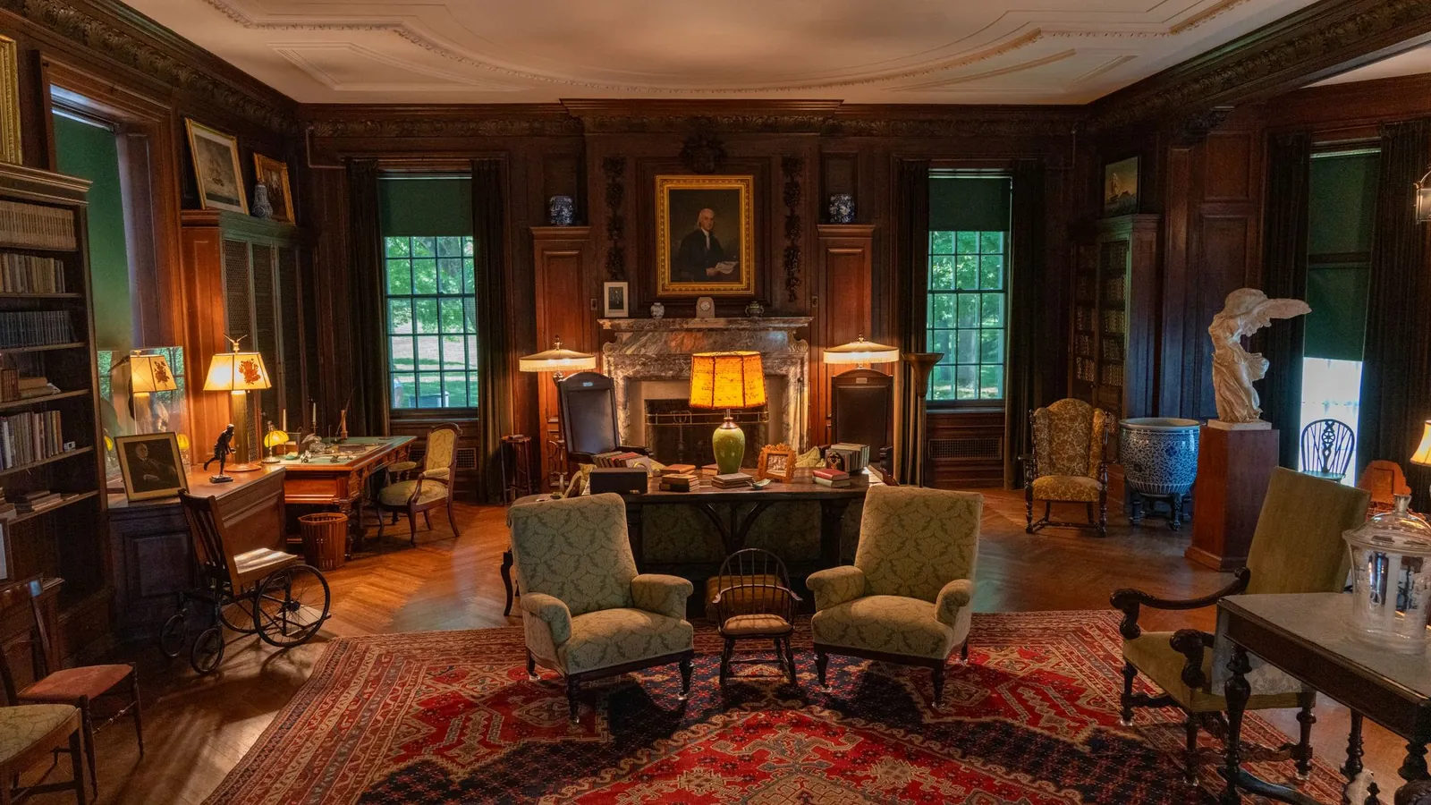Library lounge with Persian rugs, green armchairs and a lit fireplace