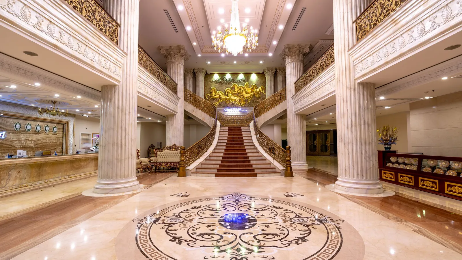 Grand marble lobby with columns, an inlaid floor and a sweeping staircase