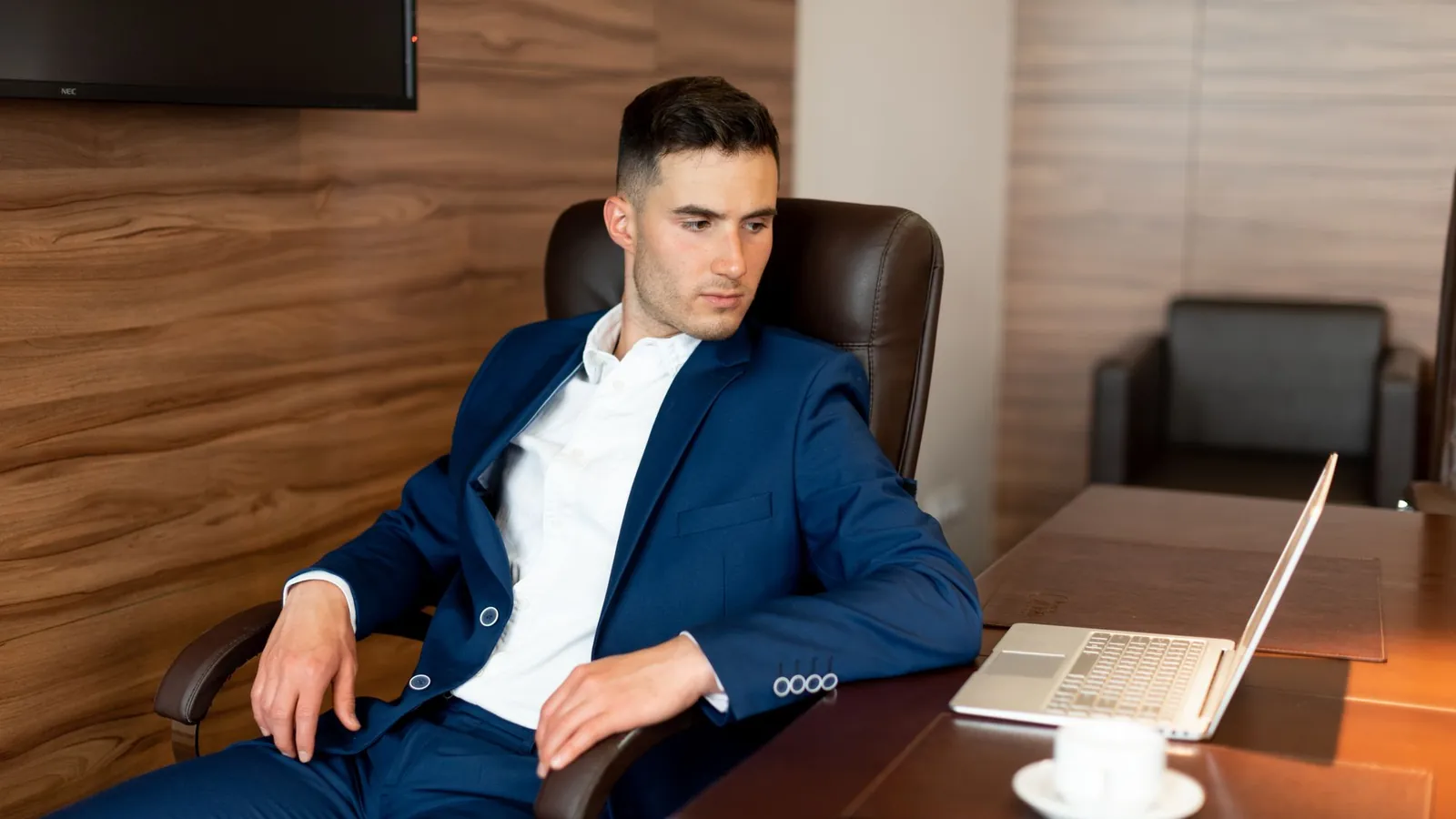 Confident professional in a navy suit seated in a leather chair in a wood-paneled office