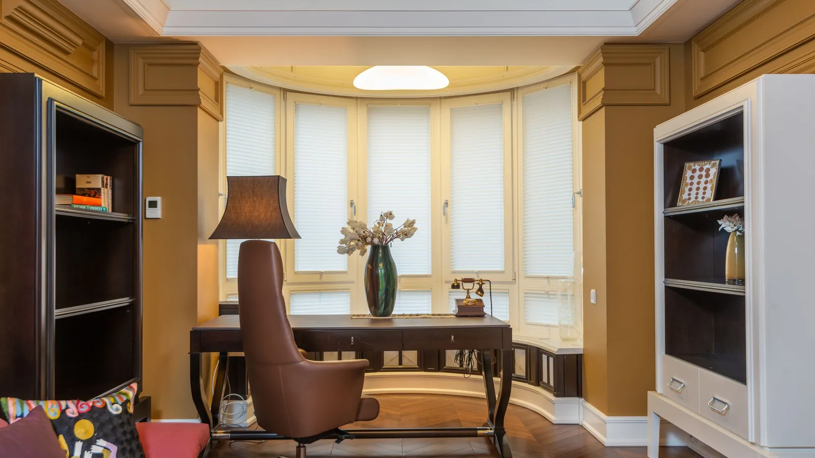 Bay-window study with a wood desk, a leather chair and bookshelves