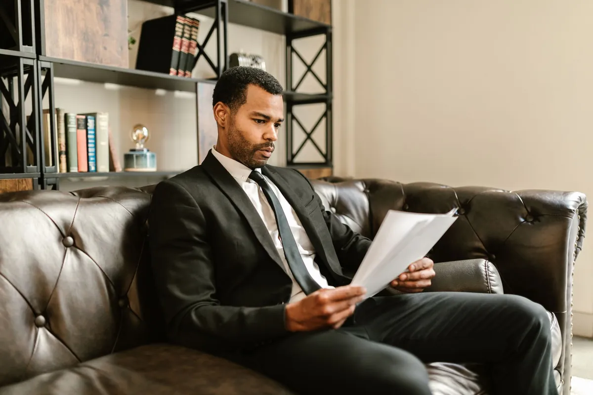 Practice owner in a suit reading a printed report in a leather armchair
