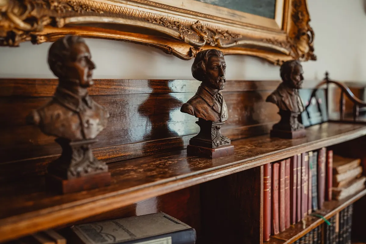 Bronze busts on a carved wood shelf beneath a gilded frame
