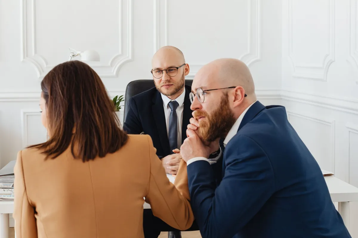 Two advisers in suits listening to a client across a white table