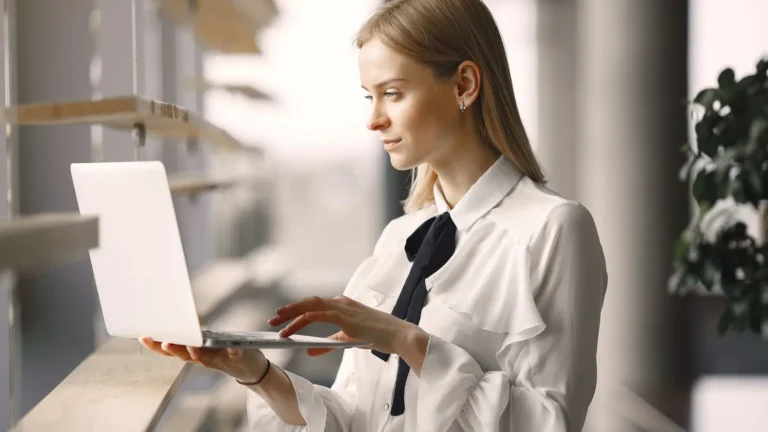 Practice owner in tailored office attire reviewing website performance on a laptop by a bright lobby window