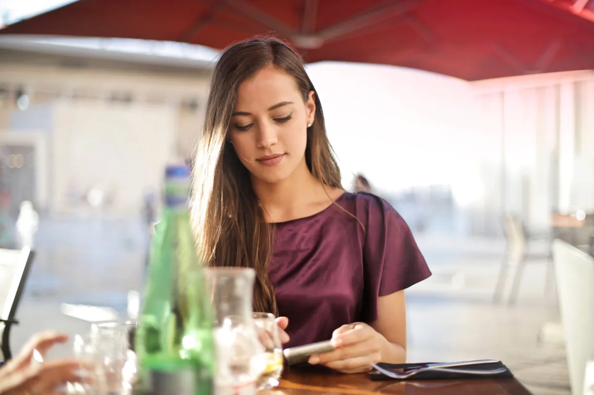 Woman in a plum blouse checking her phone at a restaurant table