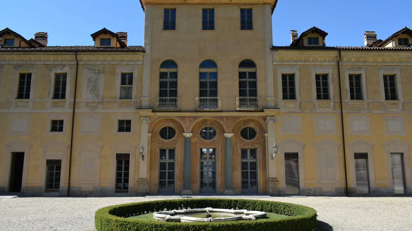 Ochre Italian villa facade with a round boxwood parterre under blue sky