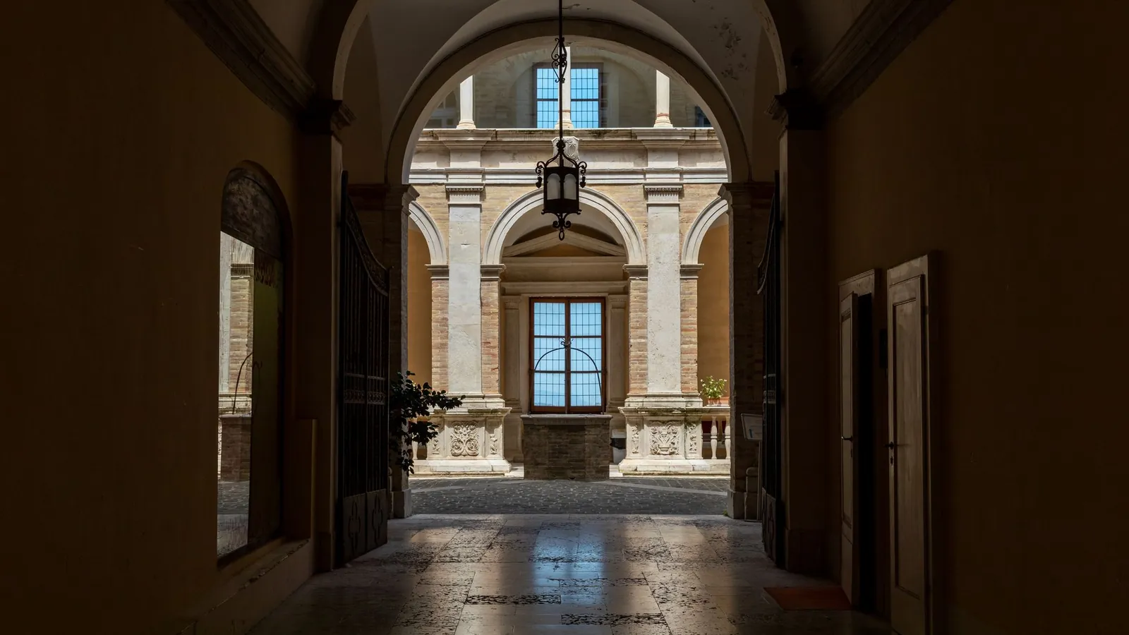 Vaulted Italian corridor opening onto a sunlit palazzo courtyard