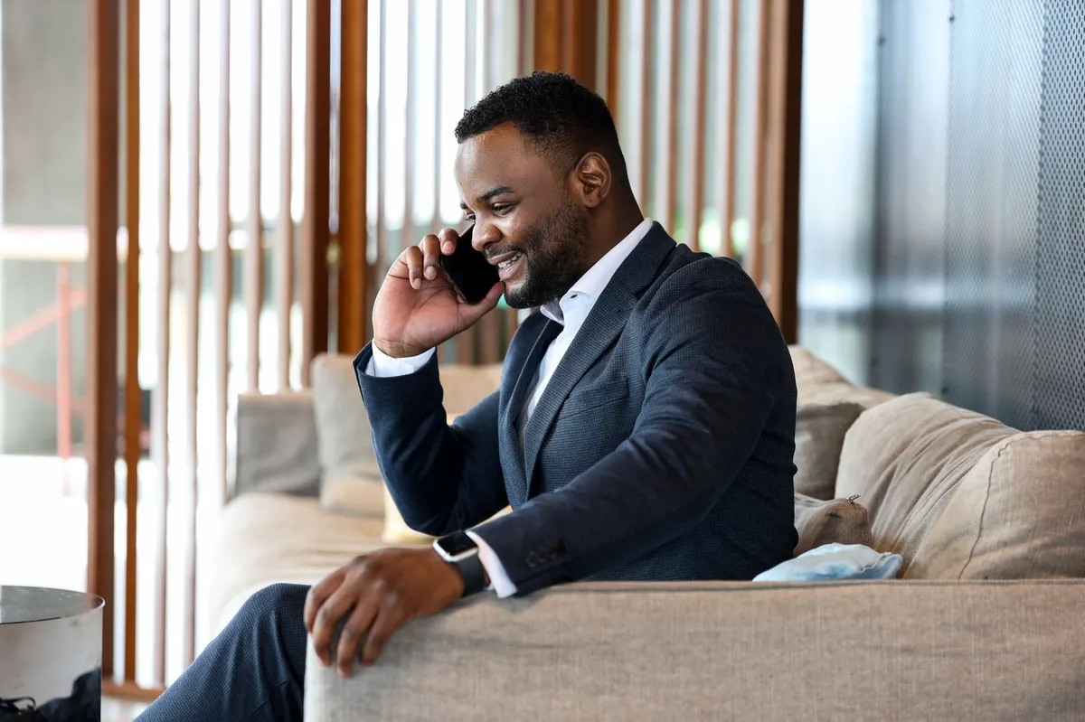 Professional in a navy suit taking a call on a sofa in a warm office