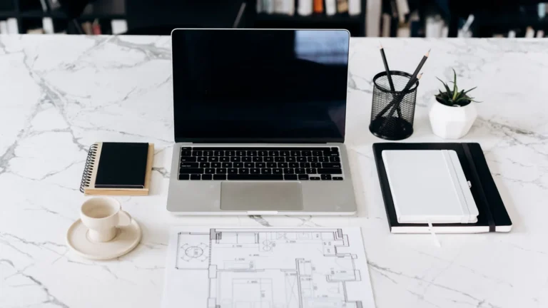 Overhead view of a laptop, phone and layout sketches on a marble desk