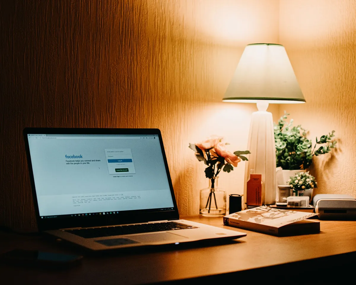 Laptop on a wooden desk beside a lamp and a small bouquet