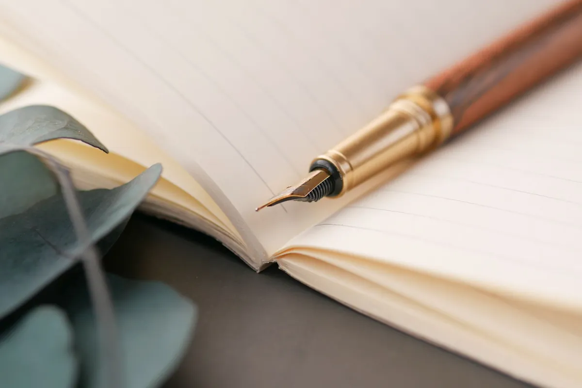 Brass fountain pen resting on the open pages of a cream notebook