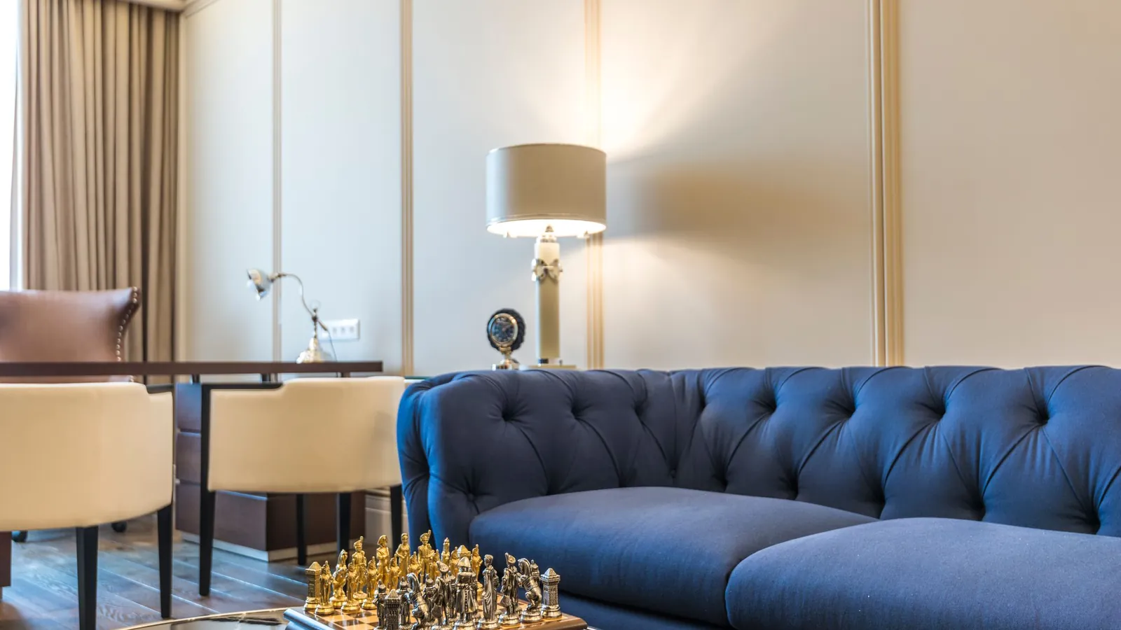 Boutique lounge with a navy tufted sofa, brass lamp and a chessboard on a coffee table