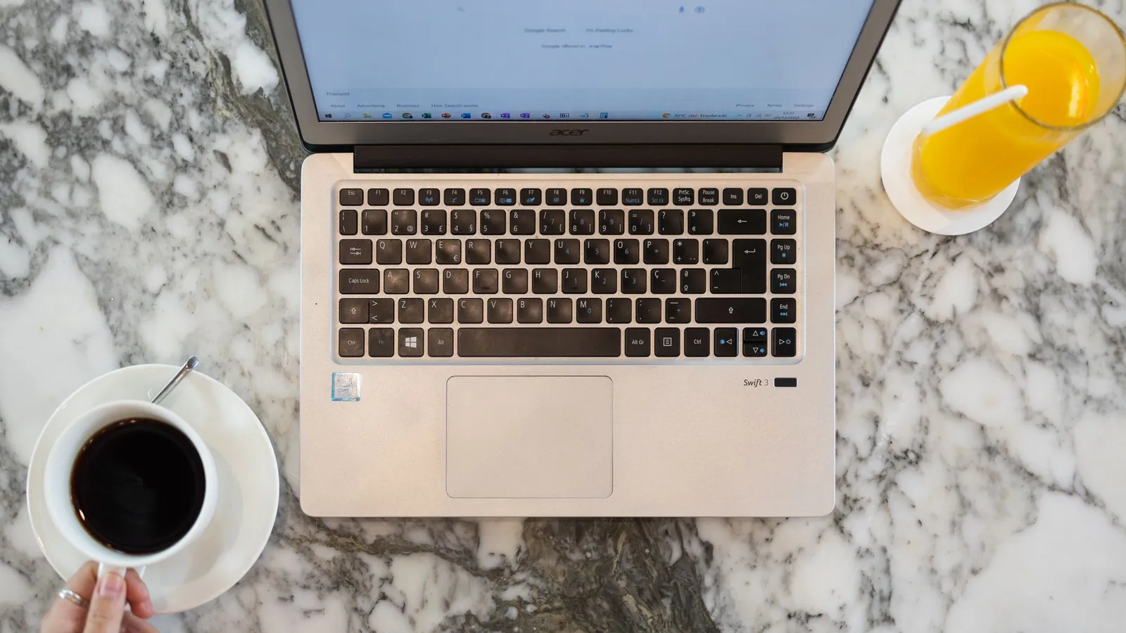Overhead view of a laptop showing a search page on a marble table with coffee