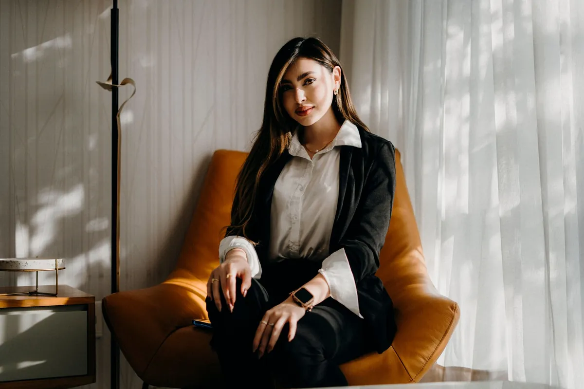 Professional in a black suit seated in a cognac lounge chair in a bright office