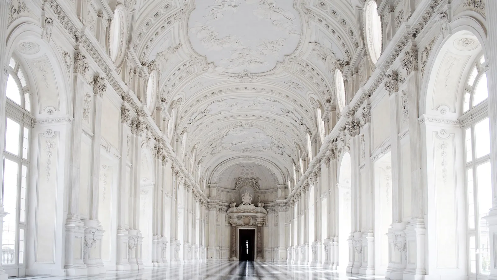 Long white palace gallery with arched windows and a polished marble floor
