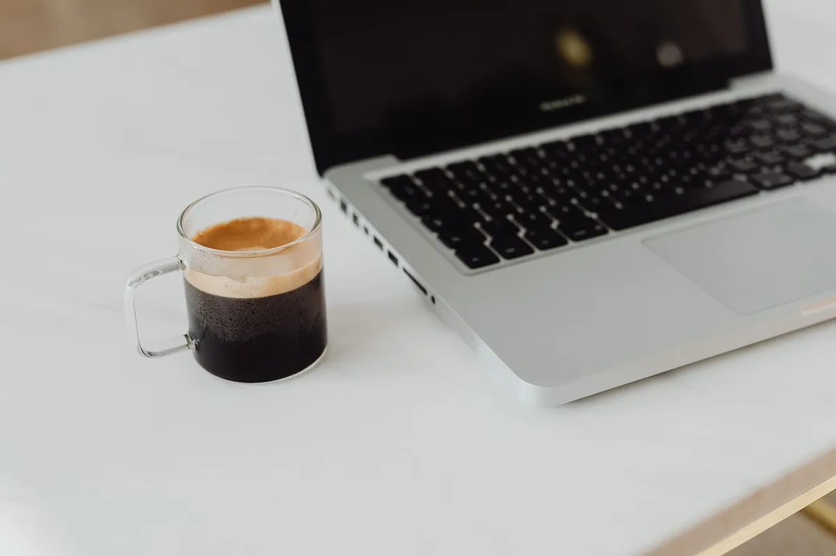 Laptop and an espresso cup on a white marble desk in soft daylight