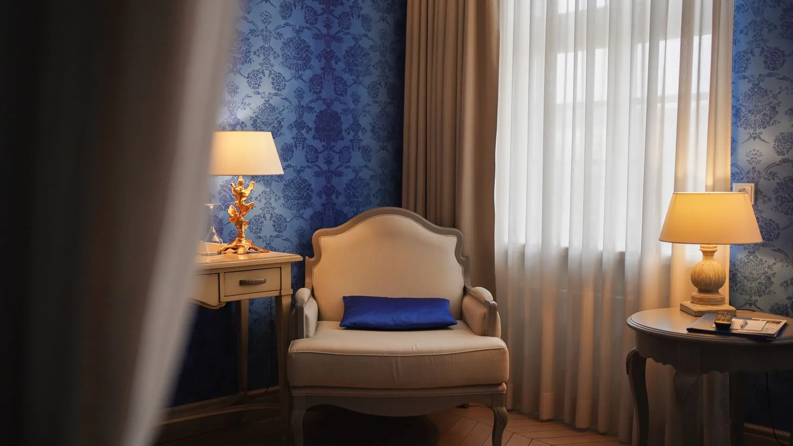 Quiet room with a cream armchair, blue damask walls and two table lamps