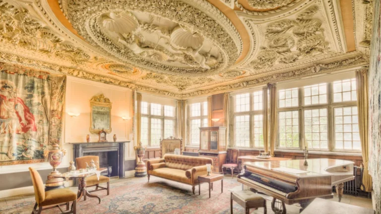 Sculpted gold ceiling over a sunlit salon with tapestries and antique sofas