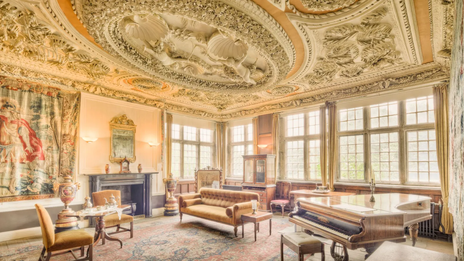 Sculpted gold ceiling over a sunlit salon with tapestries and antique sofas