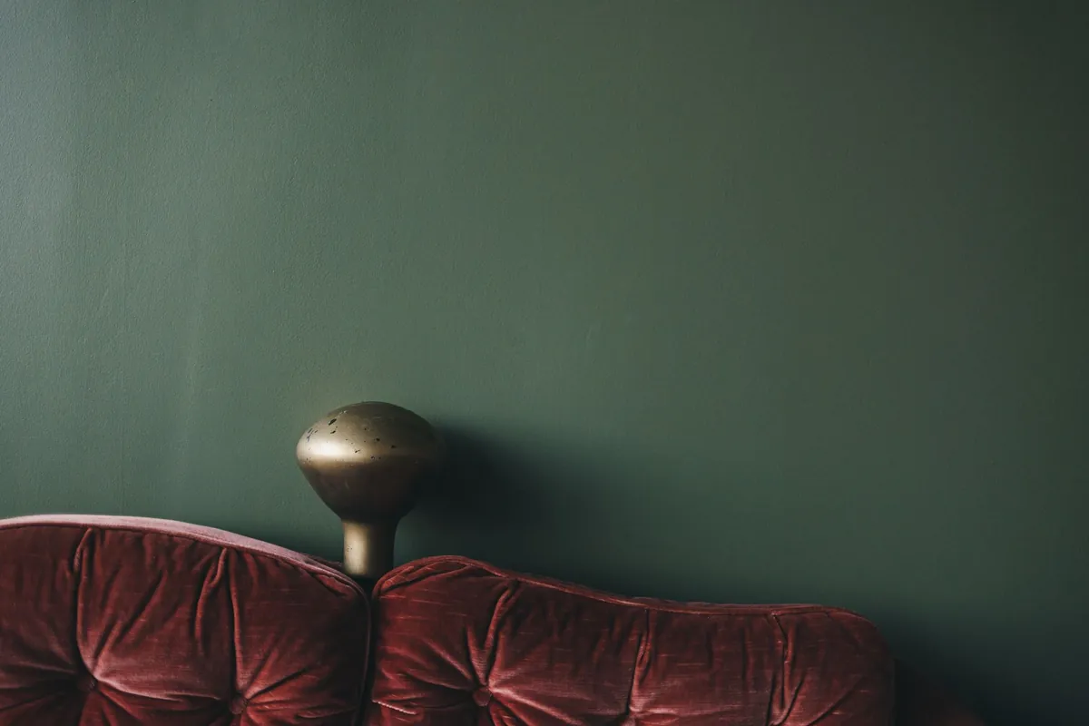Plum velvet sofa against a deep green wall with a brass lamp