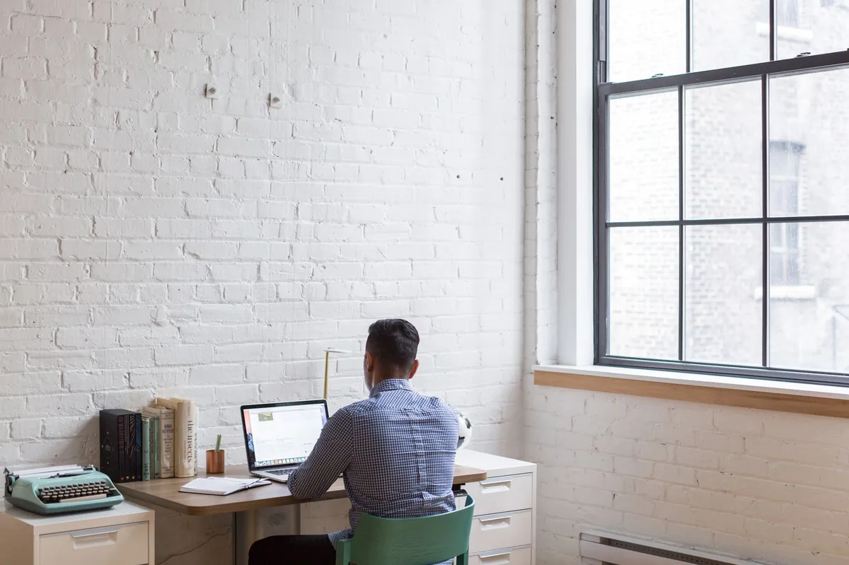 Professional working on a laptop in a well-lit home office with a large window