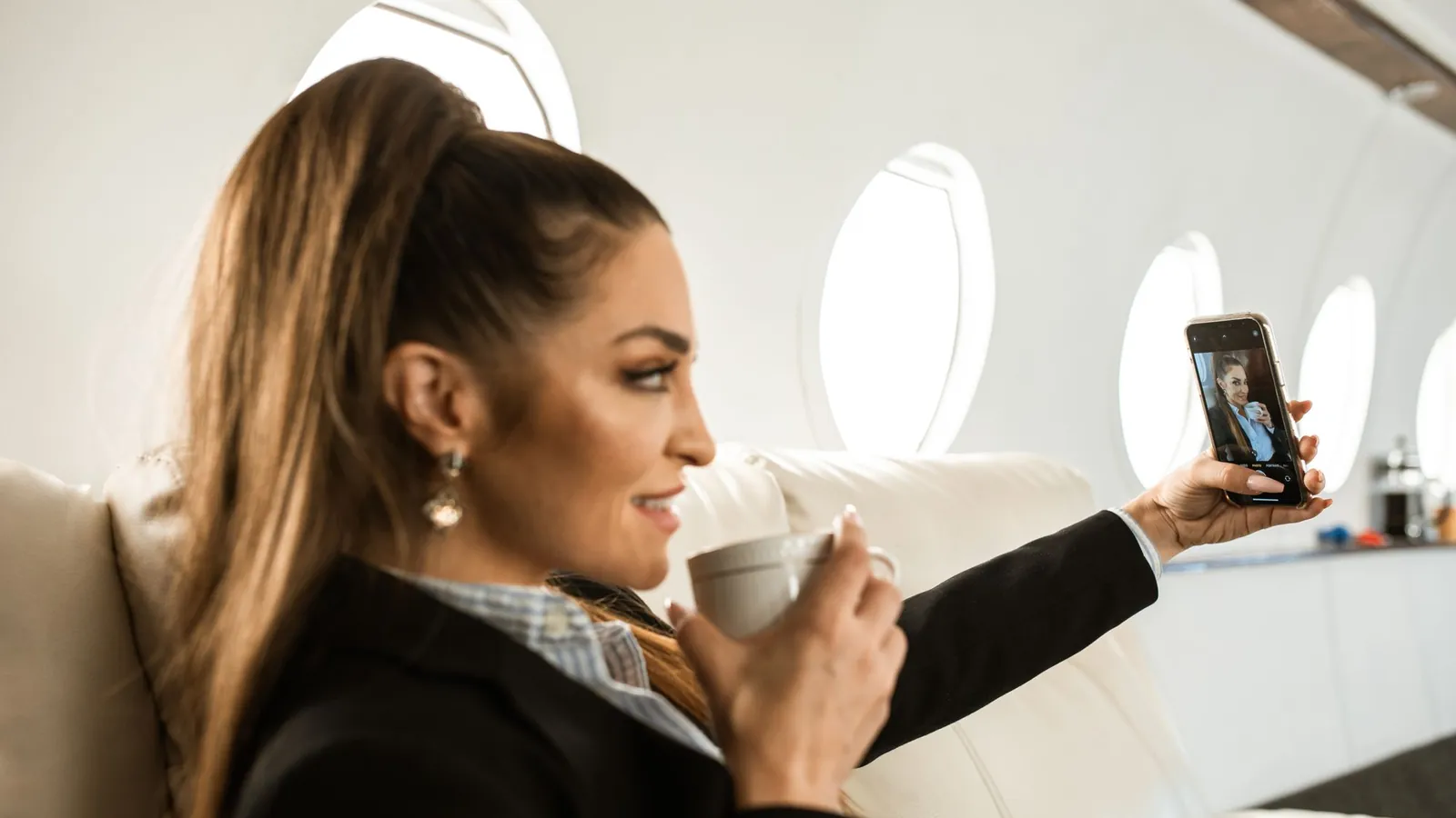Woman with a coffee taking a photo with her phone in a cream leather lounge