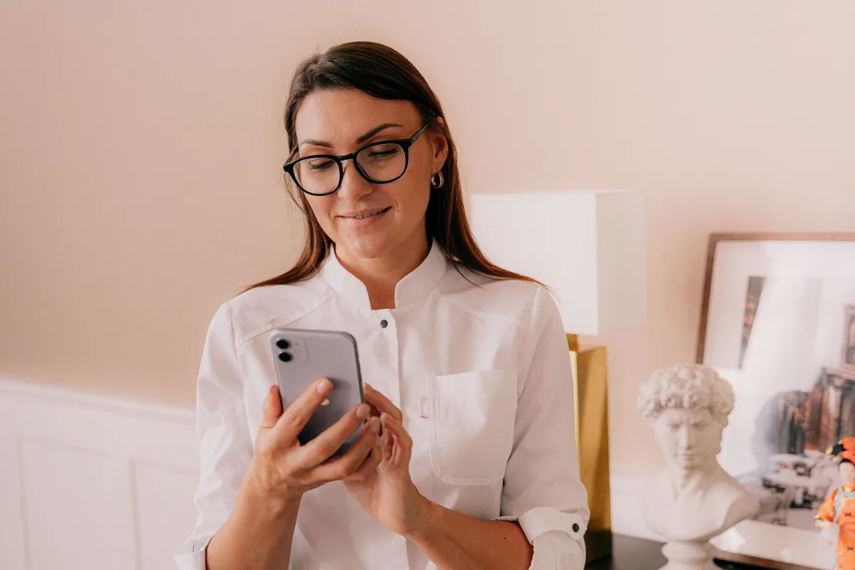 Professional in glasses and a white blouse smiling at her phone