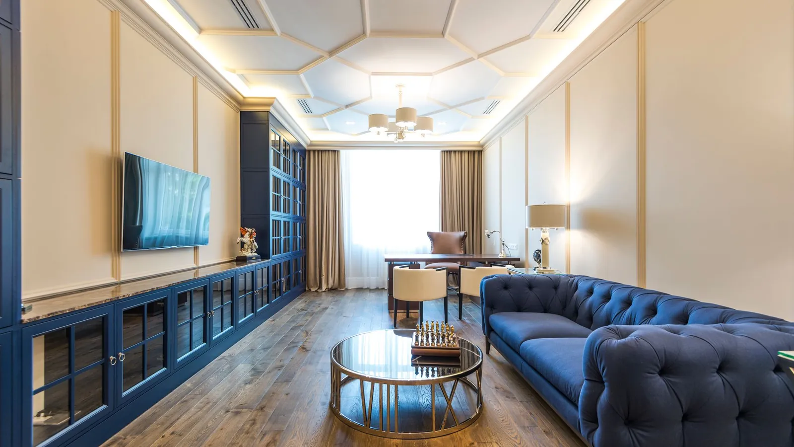 Long lounge with a navy tufted sofa, a coffered ceiling and wood floors