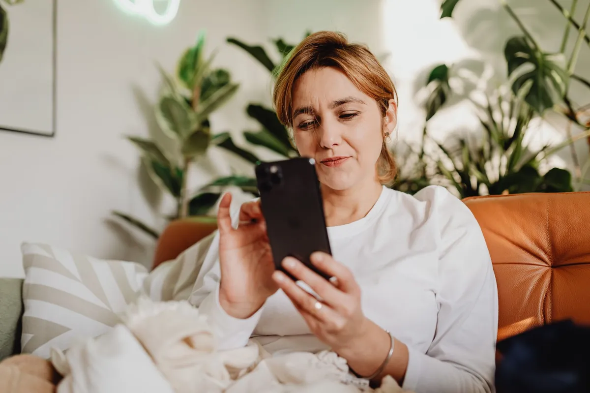 Woman scrolling short videos on her phone on an orange sofa