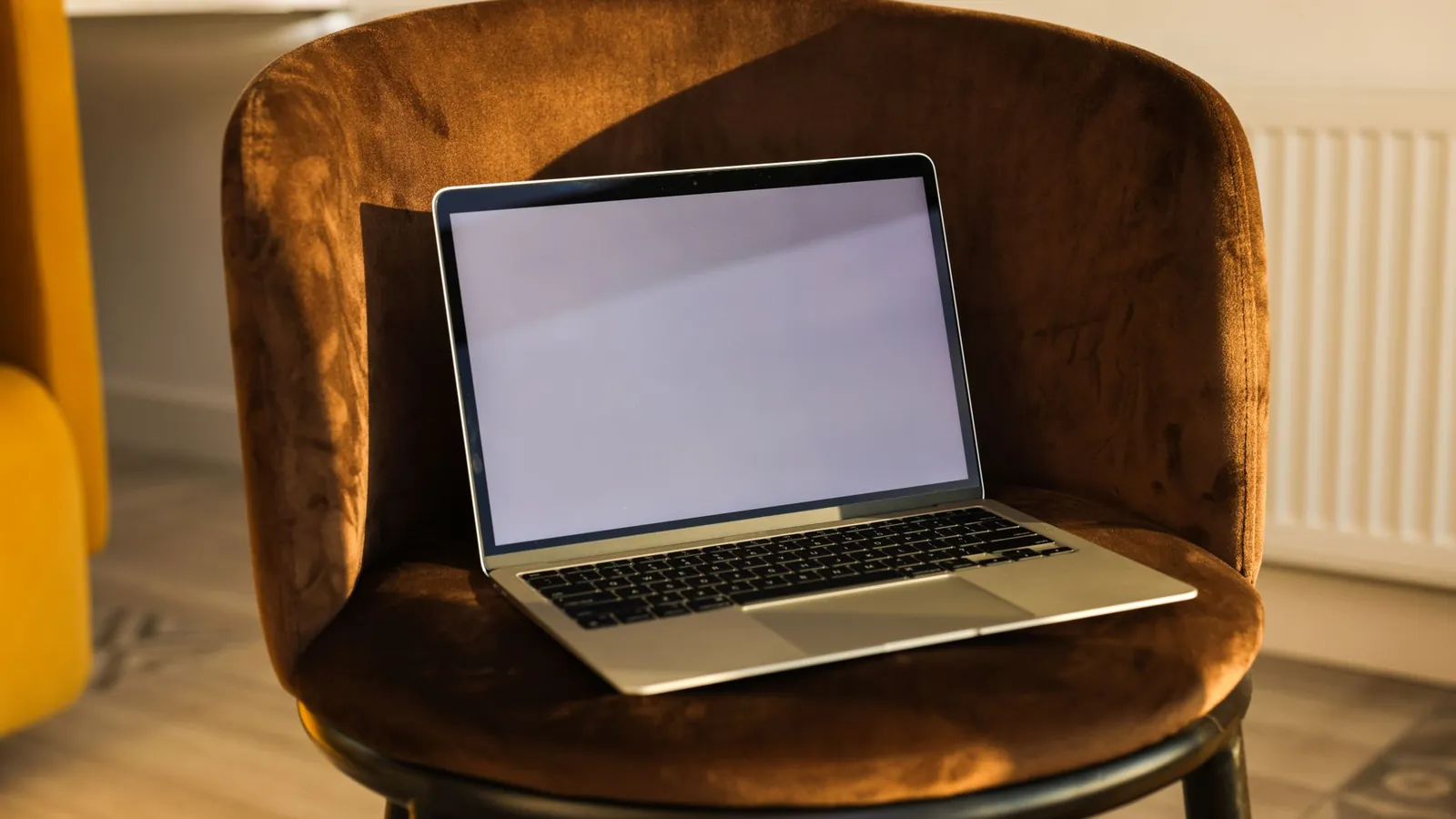 Laptop resting on a cognac velvet chair in a warm interior