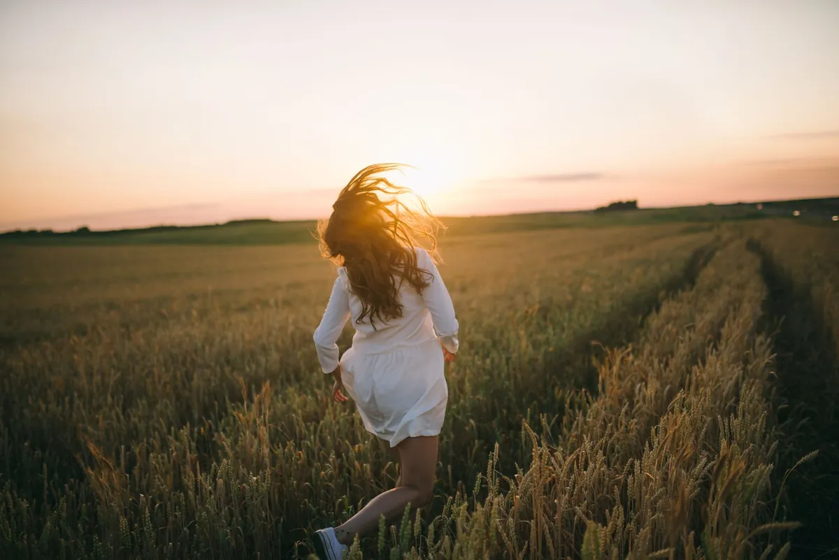 Woman running through a golden wheat field at sunset