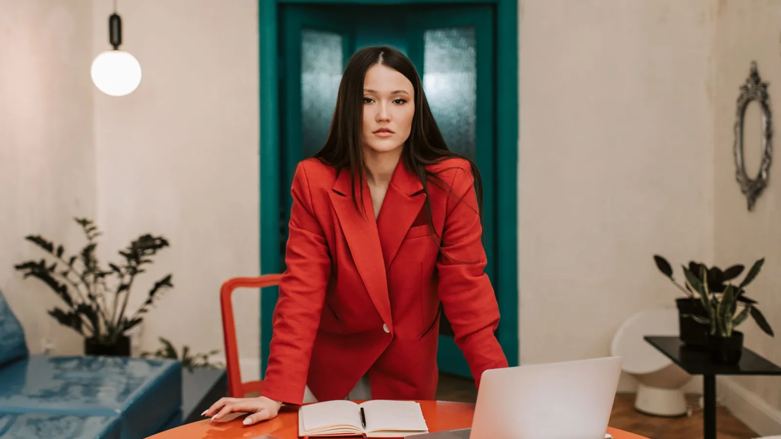 Owner in a red blazer seated at her desk in a modern office with a teal door
