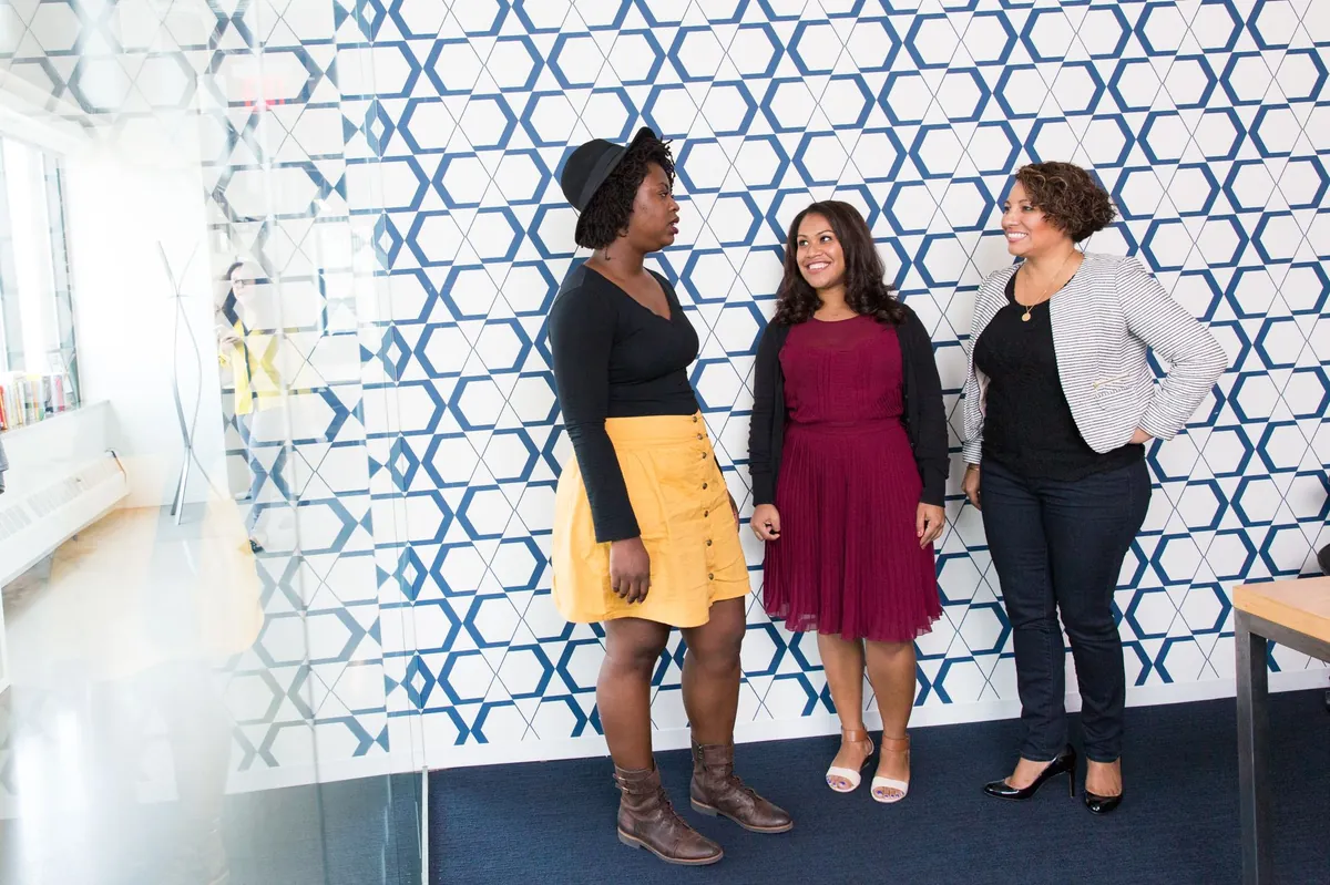Three stylish women chatting in an office with a bold geometric wall