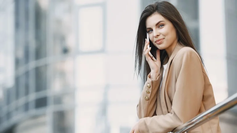 Practice owner in a camel coat taking a call on her smartphone on a city balcony