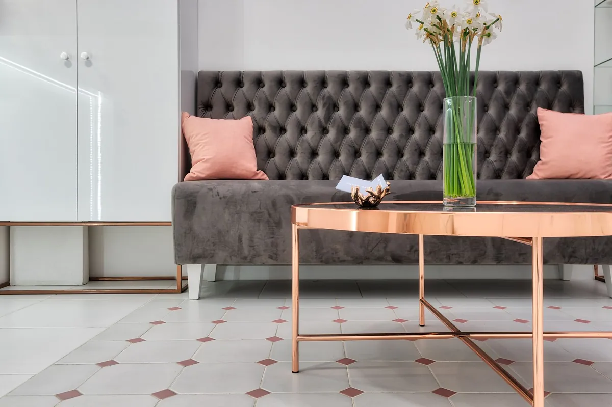 Boutique reception seating with a tufted velvet bench, blush pillows and a rose-gold coffee table