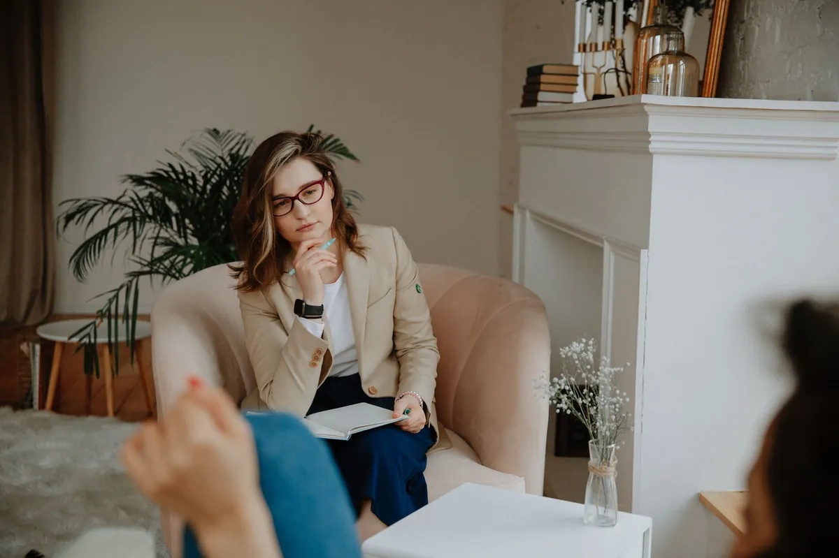 Therapist in a cream blazer taking notes during a session in an elegant, light-filled room