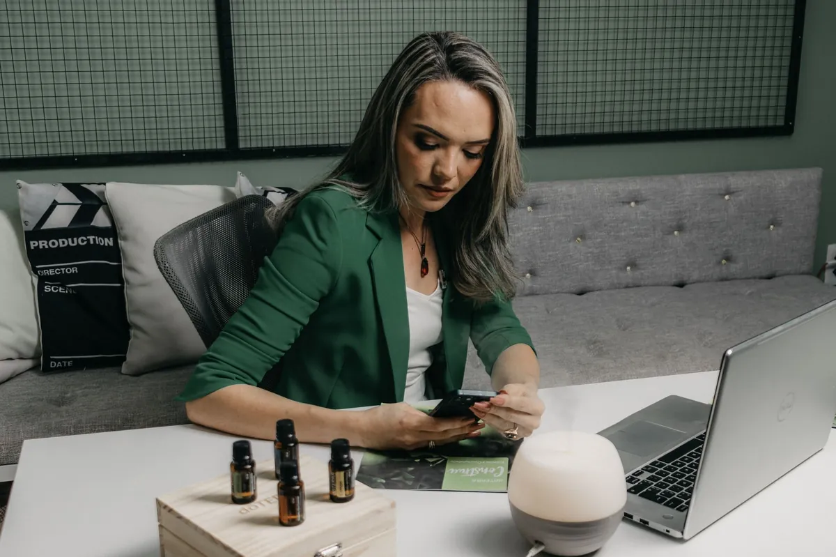 Professional in a green blazer checking her phone beside a laptop