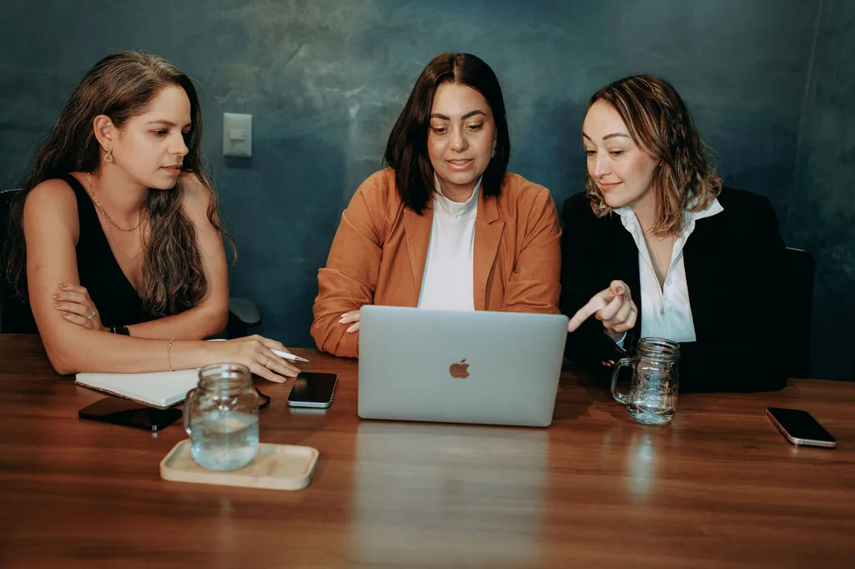 Three women in a business meeting with a laptop around a wood conference table