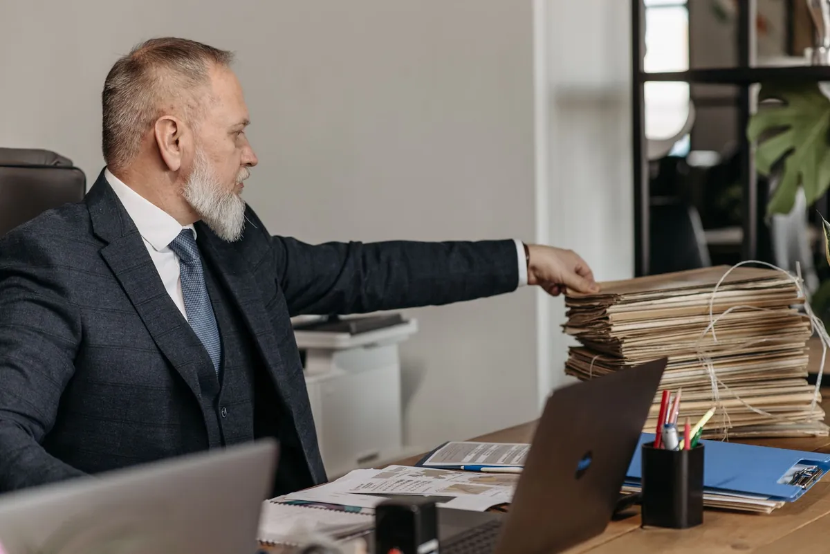 Executive in a navy suit reaching for files at a busy desk