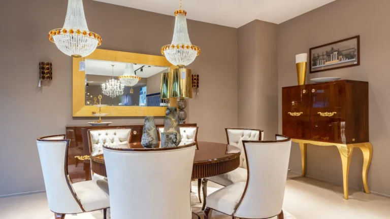 Dining room with white chairs, twin chandeliers and a gold-legged cabinet