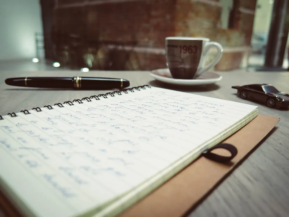 Spiral notebook with handwritten notes beside an espresso cup and a pen