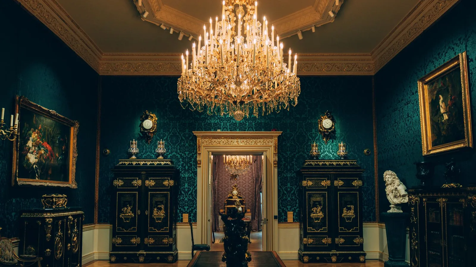 Teal gallery room with a crystal chandelier and gilded frames