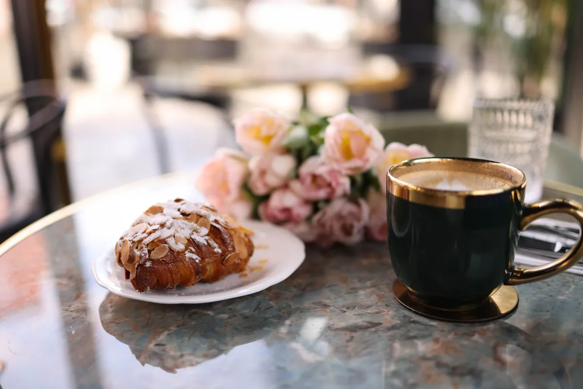 Croissant, pink roses and a gold-rimmed cup on a marble cafe table